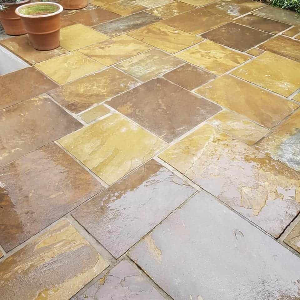 A patio with tan and brown paving and potted plants requiring exterior cleaning.
