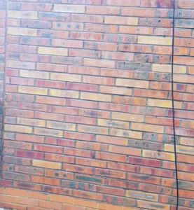 A brick wall with an attached hose for exterior cleaning.