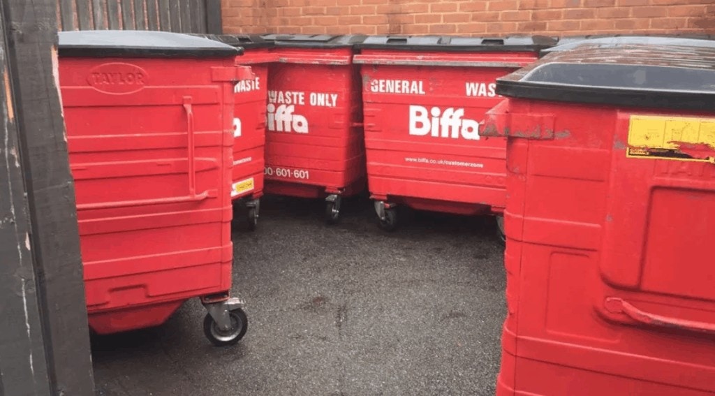 A group of red recycling bins parked in front of a brick wall, cleaned by Commercial Cleaning.