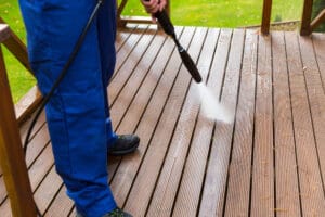 A man performing exterior cleaning on a wooden deck with a pressure washer.