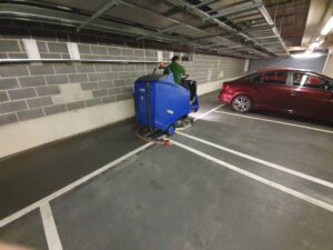 A man performing commercial cleaning in a parking garage with a blue machine.