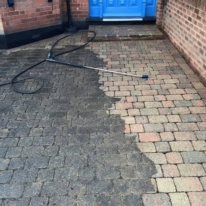 An exterior cleaning company using a pressure washer to clean a brick driveway.