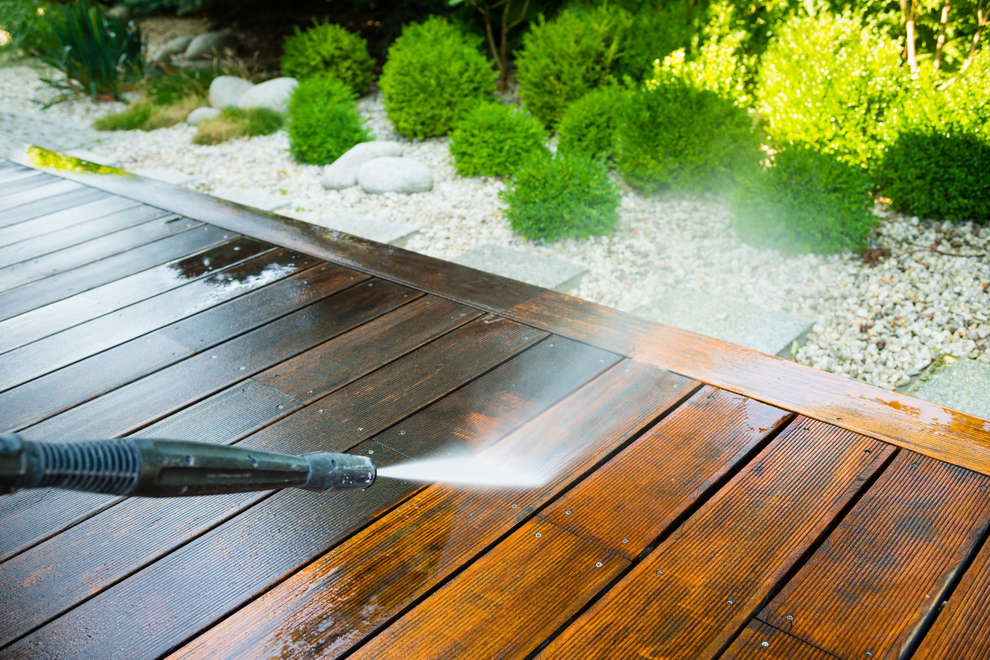 A man using a pressure washer for exterior cleaning of a wooden deck.