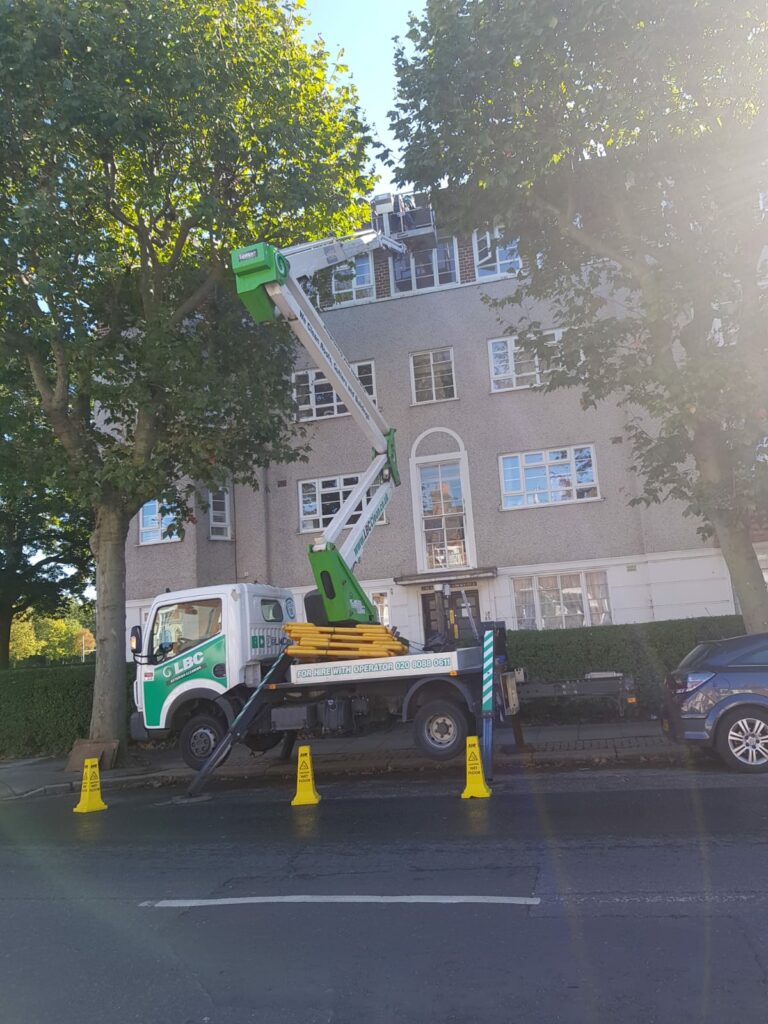 A green truck is parked in front of a building undergoing exterior cleaning.
