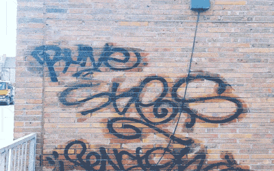 Exterior cleaning of graffiti on the side of a brick building.